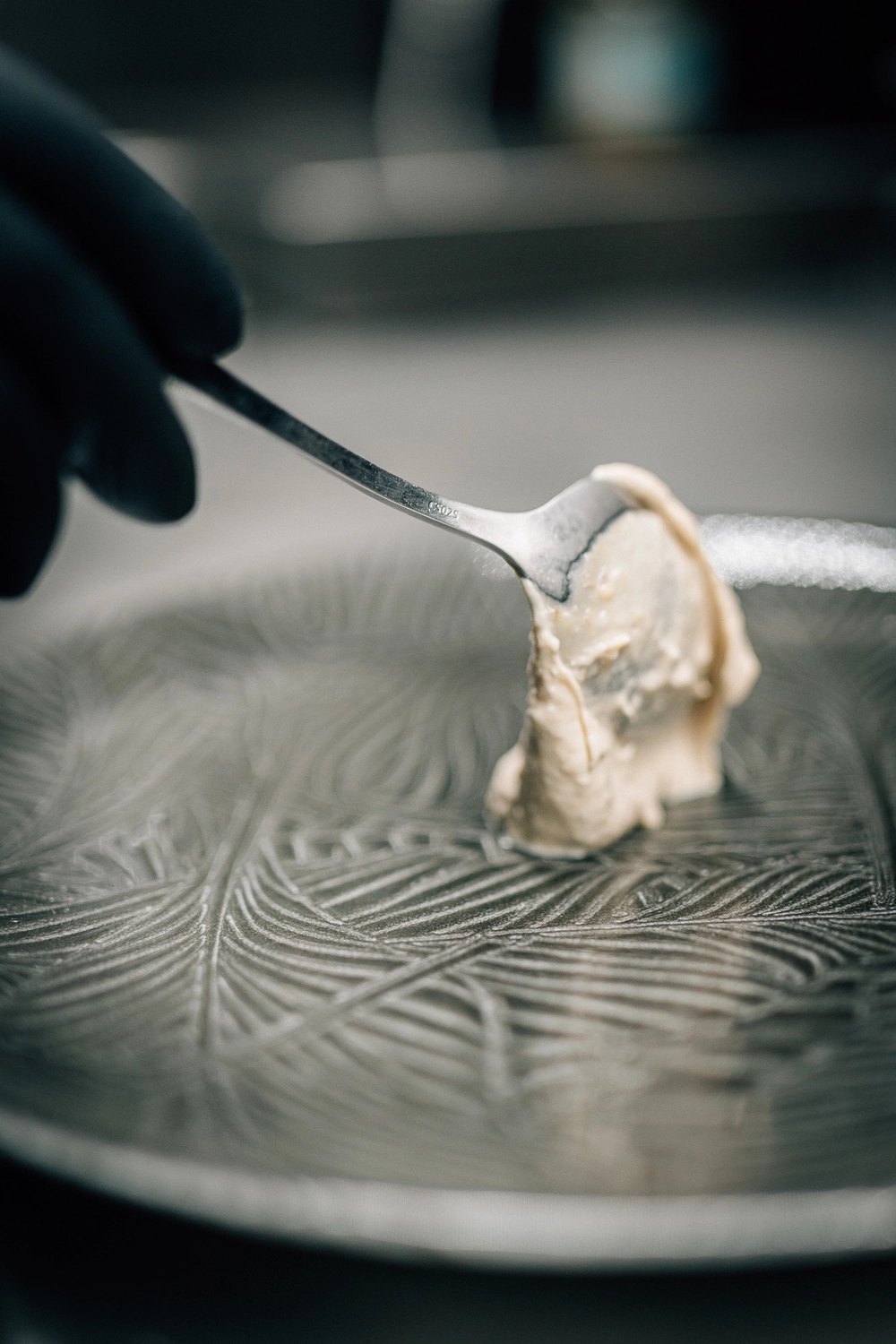 Sinn Kitchen – Restaurant – Ein Koch verteilt mit einem Löffel eine cremige Substanz auf einem kunstvoll gemusterten Teller.