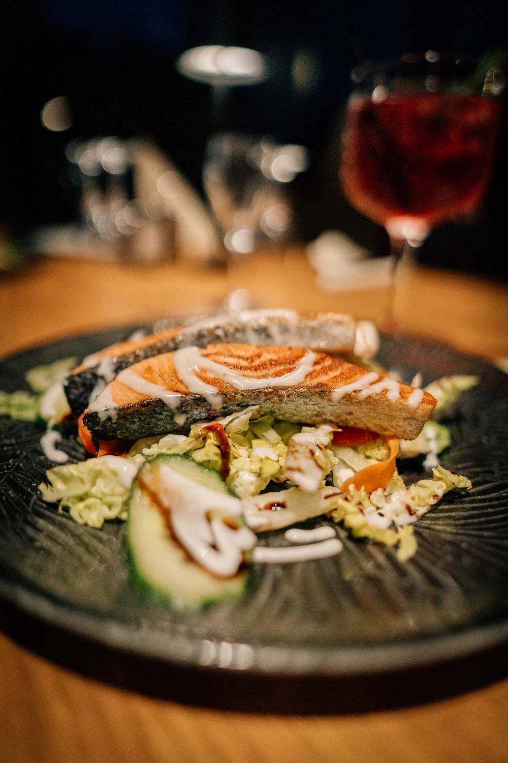 Sinn Kitchen – Restaurant – Gebratener oder gegrillter Lachs auf einem Bett aus gemischtem Salat, eventuell Salat- und Gurkenscheiben, mit einer weißen Sauce.