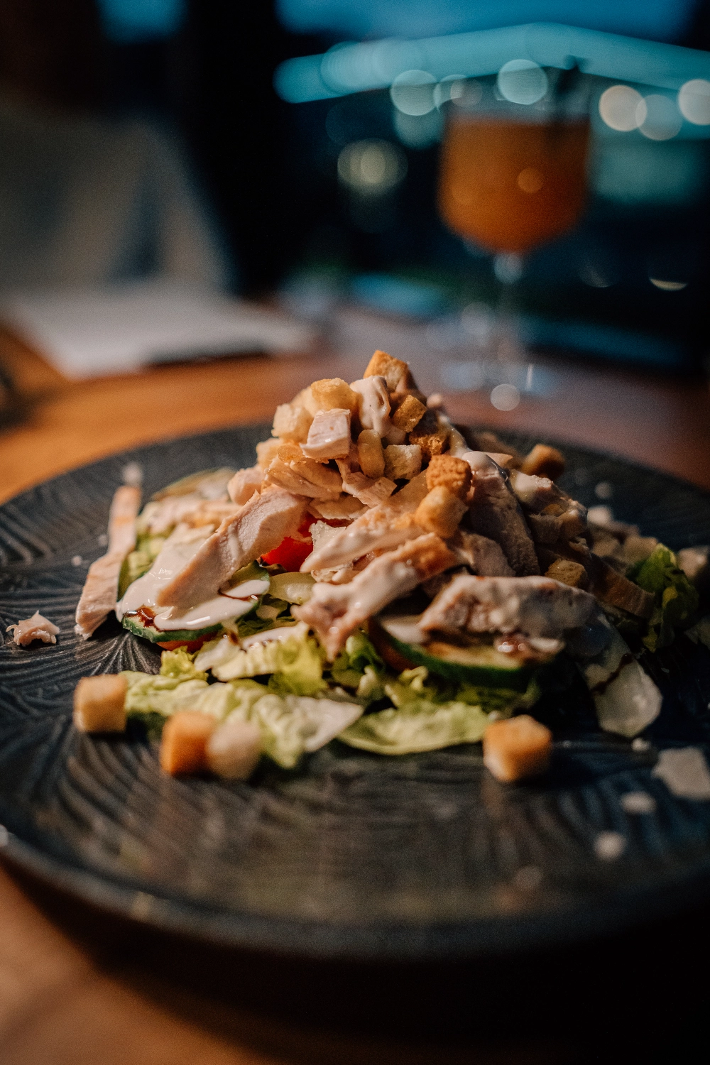 Sinn Kitchen – Restaurant – Gebratener oder gegrillter Lachs auf einem Bett aus gemischtem Salat, eventuell Salat- und Gurkenscheiben, mit einer weißen Sauce.