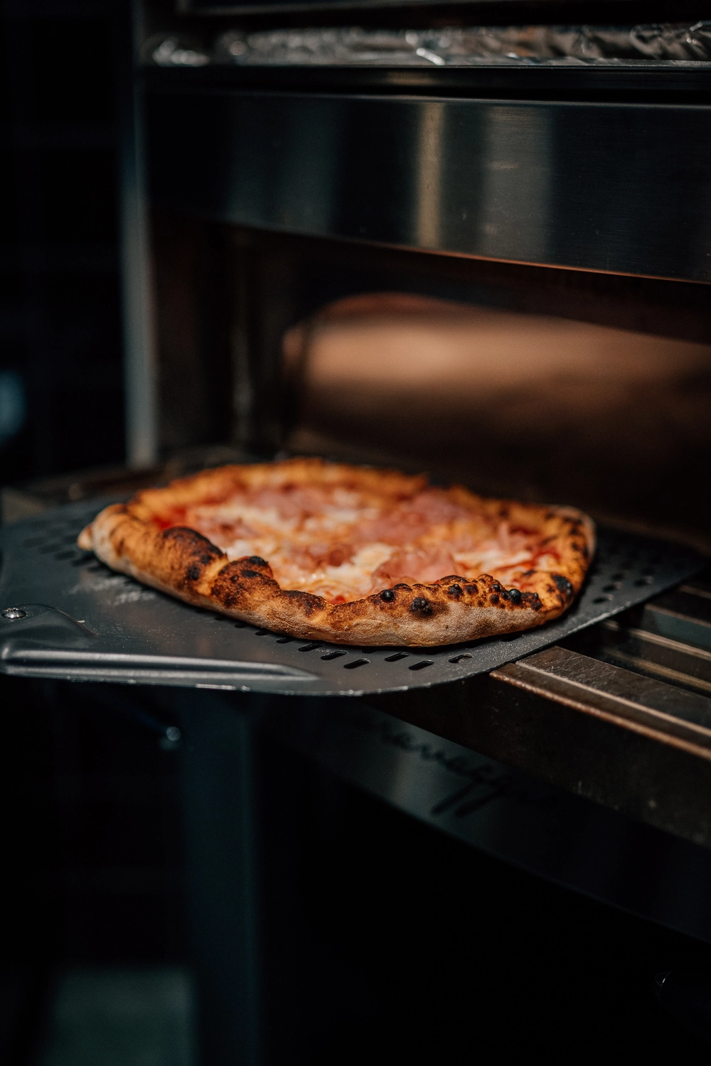 Sinn Kitchen – Restaurant – Eine frisch gebackene Pizza wird mit einem Pizzaschieber aus dem Ofen genommen.