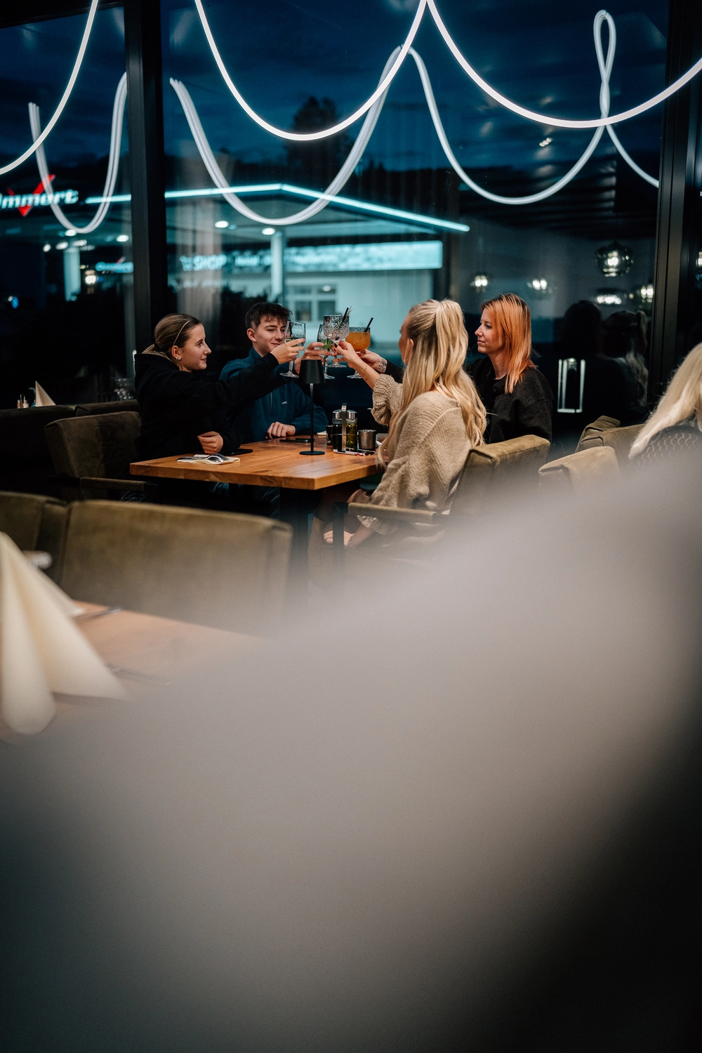 Sinn Kitchen – Restaurant – Vier junge Leute genießen ein geselliges Beisammensein in einem Restaurant oder Café am Abend. Sinn Kitchen - Restaurant -