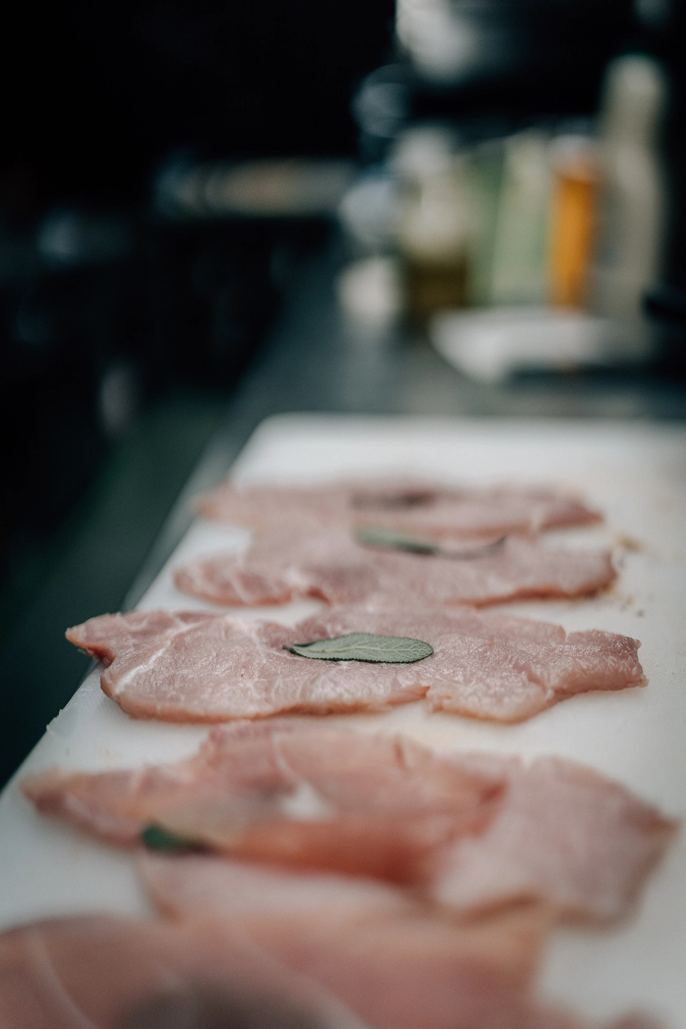 Sinn Kitchen – Restaurant – Ein Koch beträufelt dünn geschnittenes Fleisch, wahrscheinlich Bestandteil eines italienischen Gerichts wie Vitello Tonnato oder Prosciutto, mit einer Flüssigkeit, vermutlich Olivenöl oder einem Dressing.